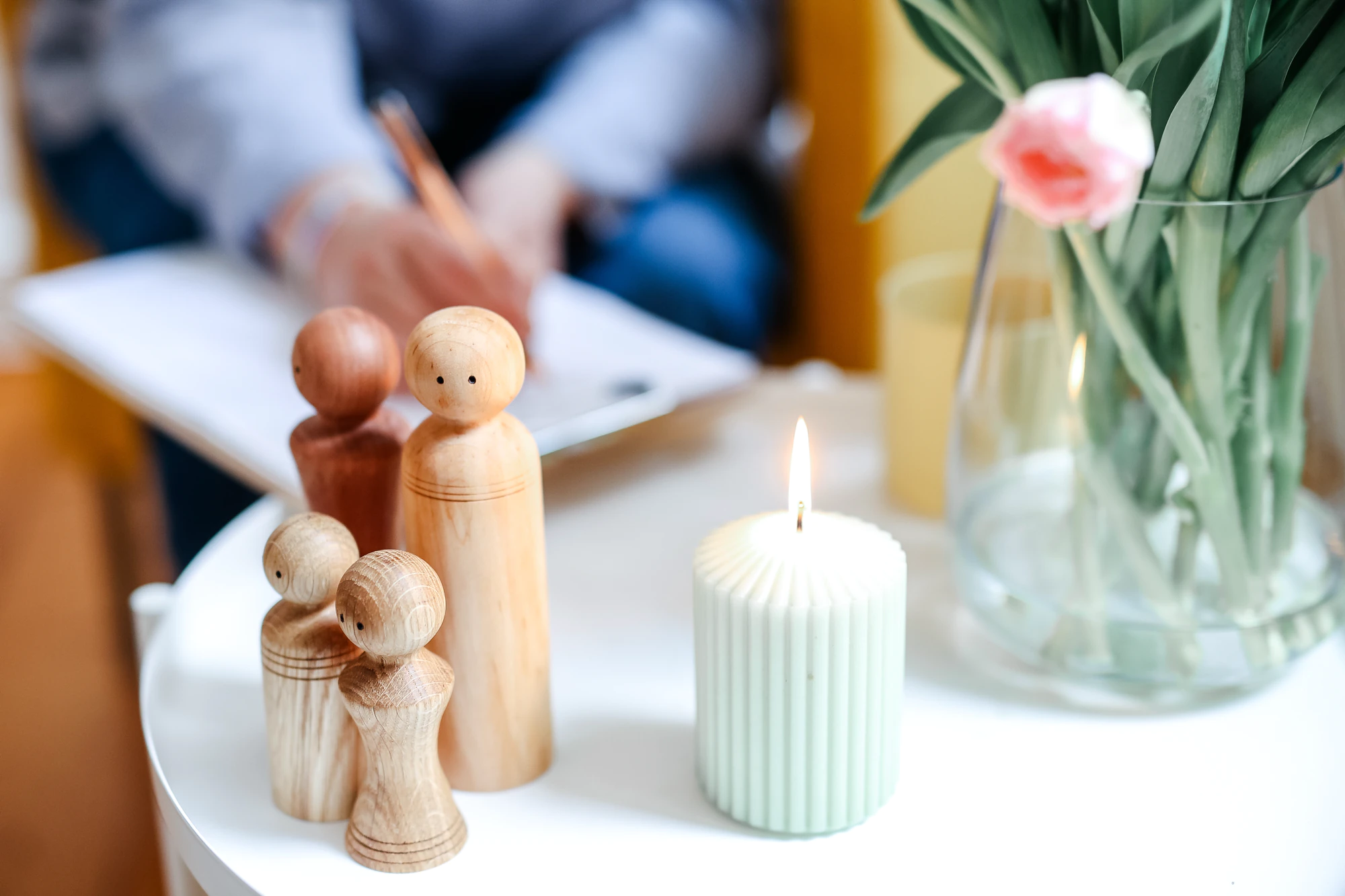 Drei Holzfiguren neben einer Kerze und Blumen als Symbol für Beziehungsmuster