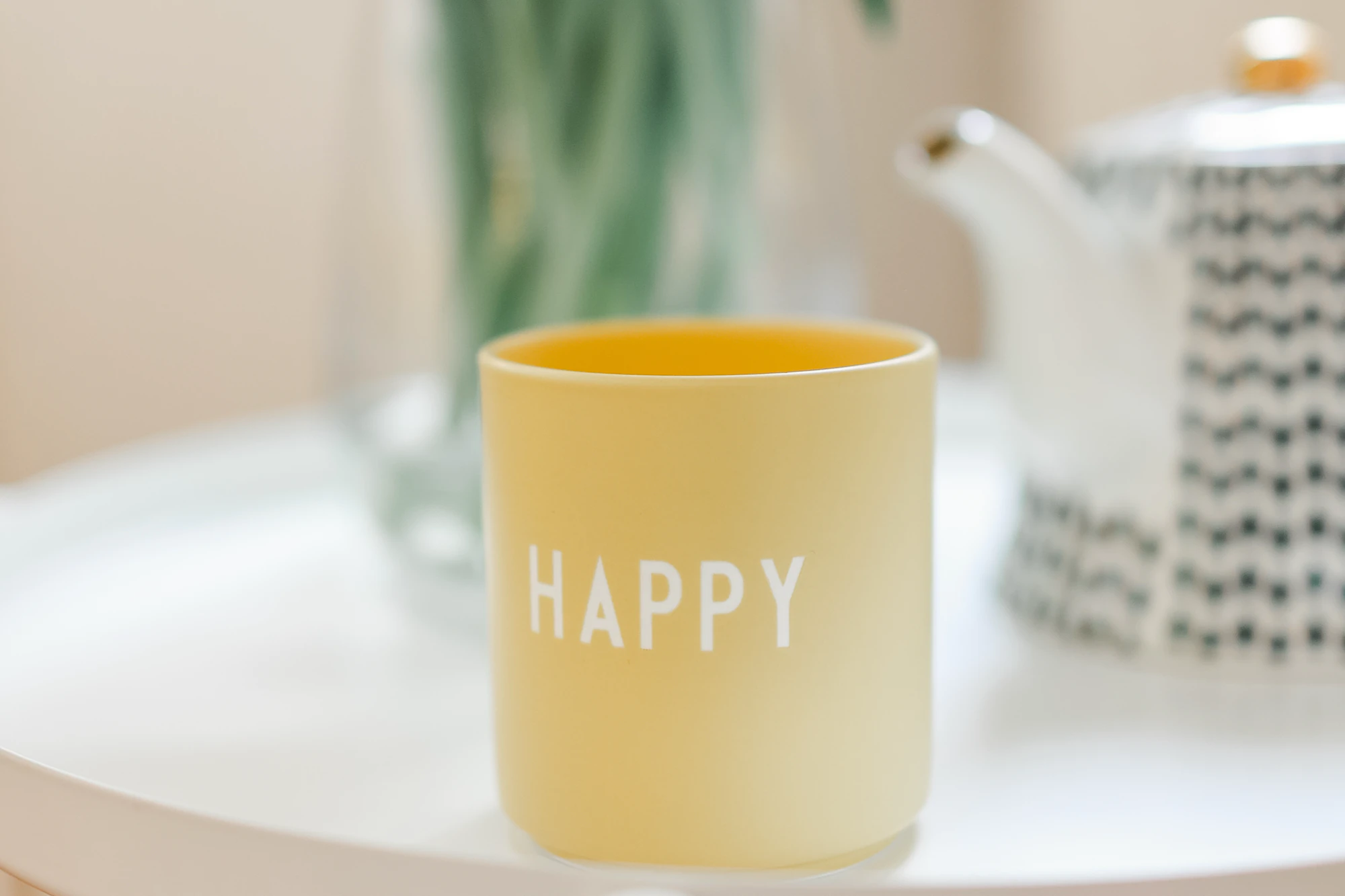 Gelbe Tasse mit der Aufschrift Happy auf einem Tisch im Praxisraum
